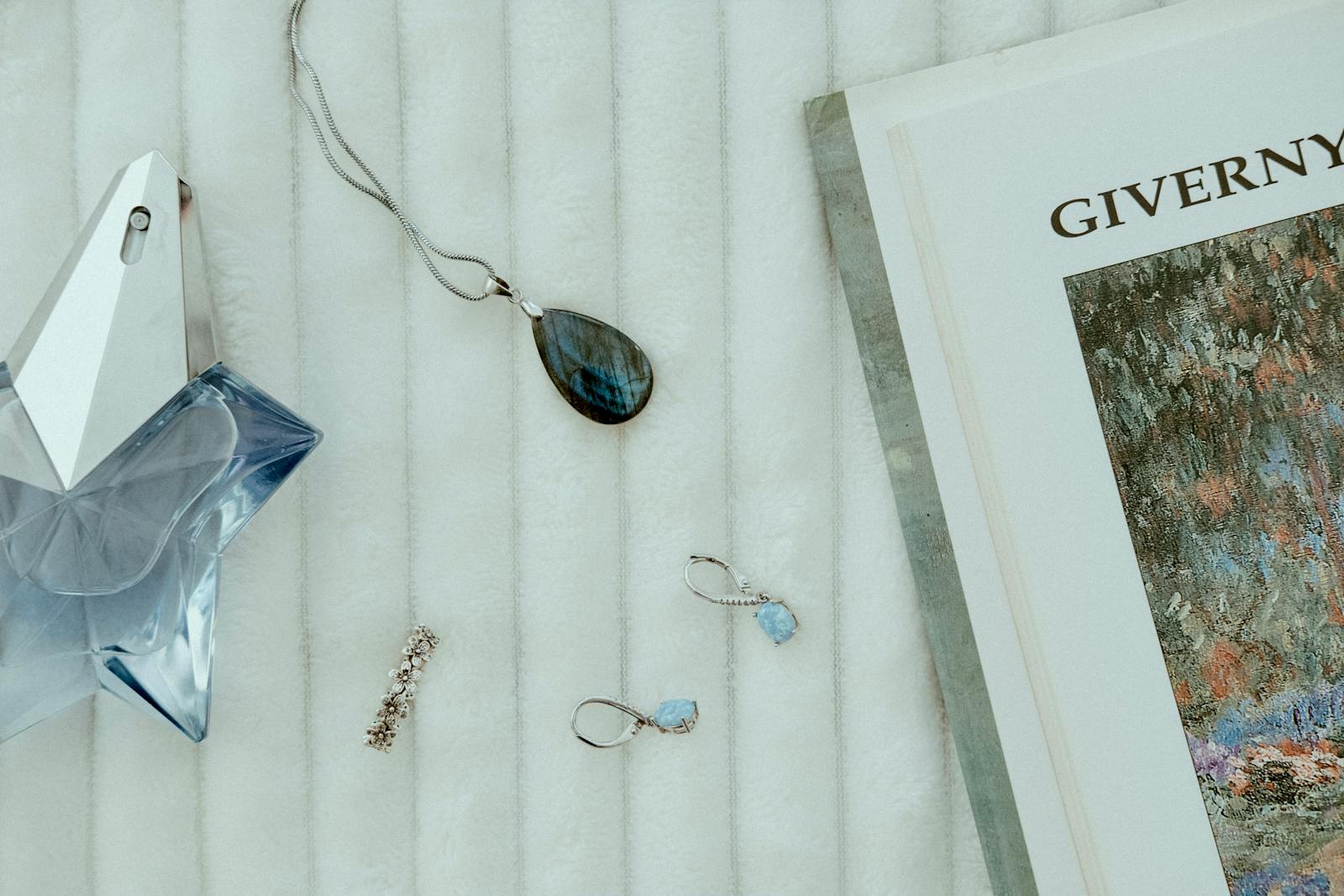 Flat lay of jewelry, a perfume bottle, and a book on a soft surface, creating a luxurious ambience.